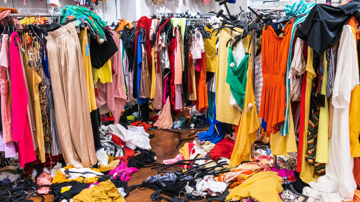 Colorful garments on racks and on the floor; fast fashion concept