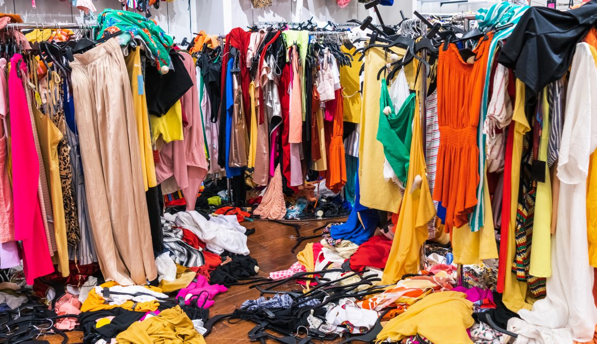 Colorful garments on racks and on the floor; fast fashion concept