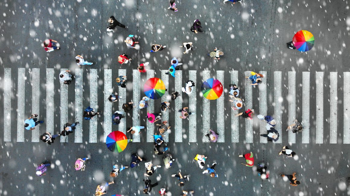 Aerial. People crowd on a pedestrian crossing crosswalk when it’s rain. View above.