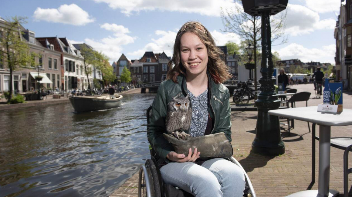 Jiska Ogier zit op een kade. Achter haar vaart een boot en staan huizen. Met een leren handschoen aan haar rechterhand houdt ze een uil vast.